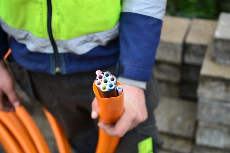 Supervisory road worker shows 9 hollow tubes in an orange pipeline used to blow in fiber optic wires. 2 outdoor pipes used for connection to the house